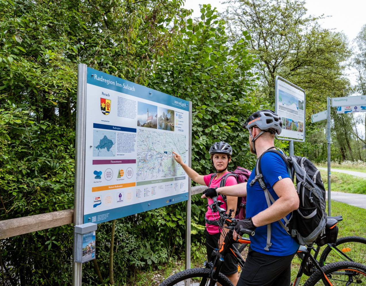 Zwei Radfahrer stehen vor einer Rad-Infotafel der Region Inn-Salzach, eine Person zeigt auf die Infotafel, © Gregor Lengler